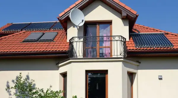 Elegancki wykusz co to? To część domu wystająca na zewnątrz, z oknami i balkonem, na dachu kolektory słoneczne.