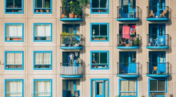 Elegancka loggia i balkon z niebieskimi ramami okiennymi, pełne zieleni i suszącego się prania, tworzą barwną fasadę budynku.