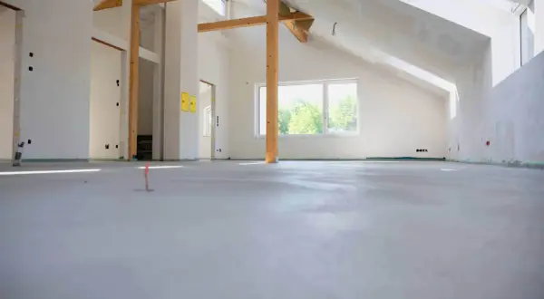 Nowe wnętrze z drewnianymi belkami i oknem. Podłoga gotowa pod wykończenie, zastanawiasz się, ile za metr wylewki?