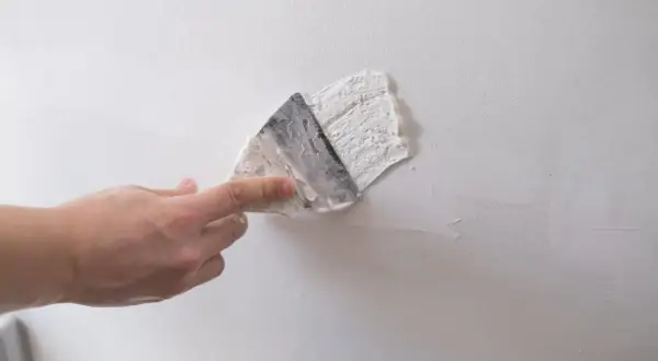 Dłoń zacierająca gips szpachlowy na białej ścianie. Czas, ile schnie gips szpachlowy, zależy od warunków.