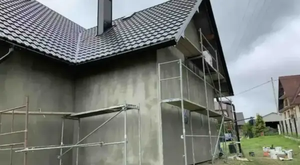 Dom w trakcie prac elewacyjnych. Rusztowanie wokół budynku, szara ściana. Sprawdź elewacja cena za m2 robocizna.