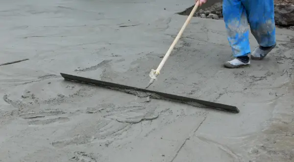 Robotnik w niebieskich spodniach wyrównuje świeżą wylewkę miksokretem.