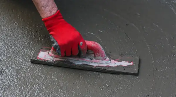 Dłoń w czerwnej rękawicy wygładza mokrą wylewkę pacą.