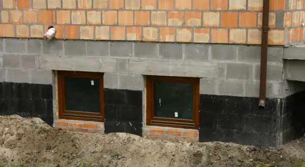Budowa fundamentu pod starym domem: widok na ściany z pustaków, okna piwniczne i izolację przeciwwilgociową.