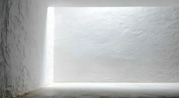 Białe, chropowate ściany i sufit w minimalistycznym wnętrzu z jasnym światłem.