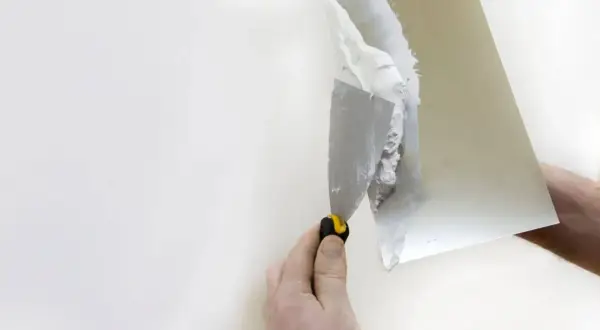 Nakładanie gładzi na karton gips. Ręka trzymająca kielnię z masą szpachlową, przygotowuje ścianę do malowania.