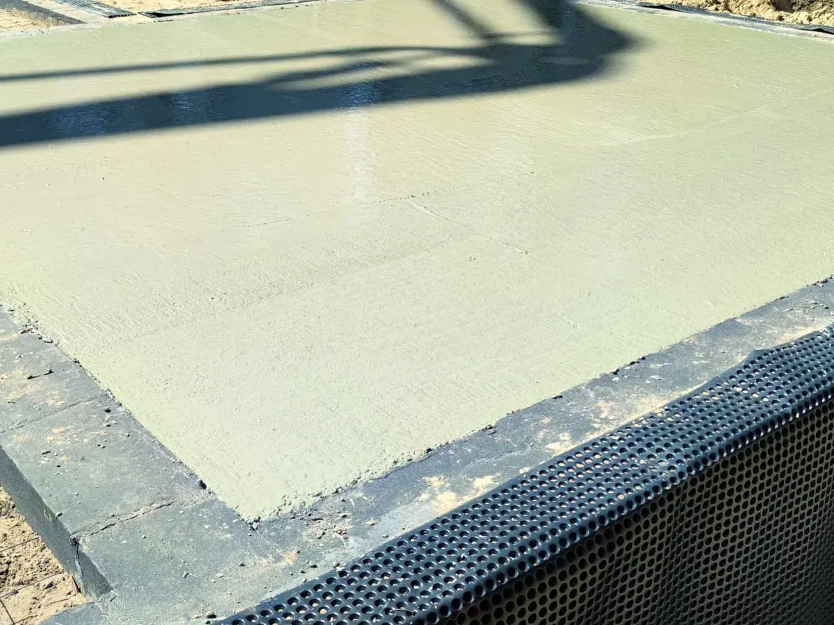 Świeżo wylany beton na budowie. Powierzchnia jest gładka, a cień rzucany przez coś na górze przypomina chudziaka.