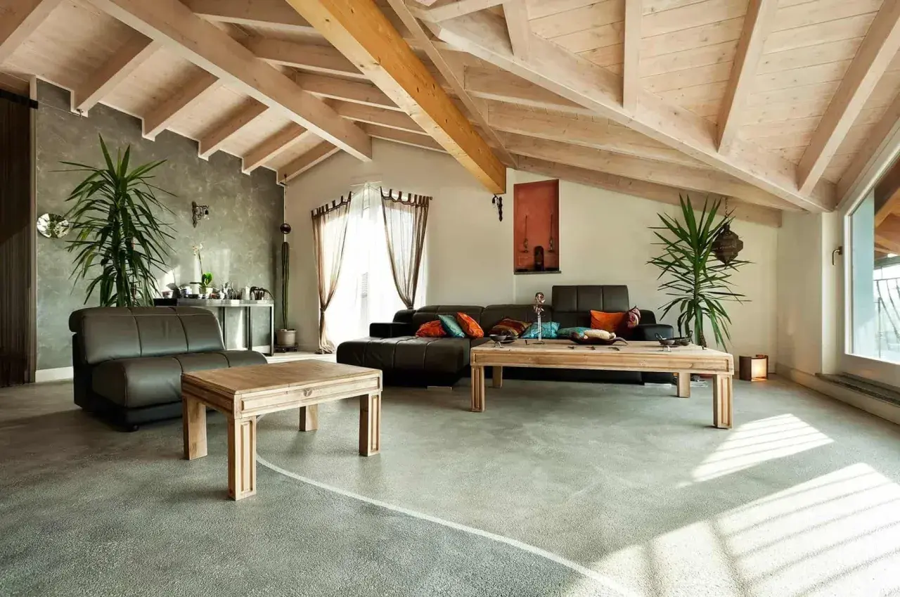 Nowoczesny salon z podłogą z żywicy, która ma pewne wady, ale dodaje wnętrzu charakteru. Drewniane belki na suficie i jasne meble tworzą przytulną atmosferę.