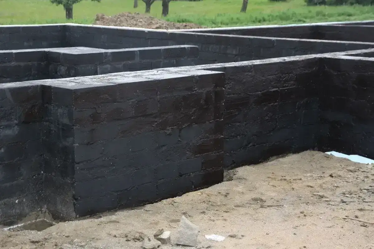 Fundament z czarnej cegły, przygotowany do izolacji. Widać, że prace postępują, a fundamenty są już prawie gotowe, co pozwala disprobit na dalsze etapy budowy.
