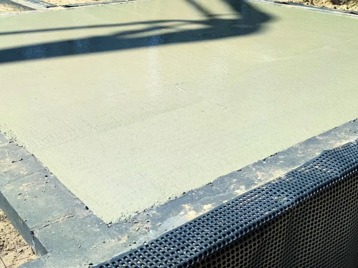 Świeżo wylany beton na budowie. Powierzchnia jest gładka, a cień rzucany przez coś na górze przypomina chudziaka.