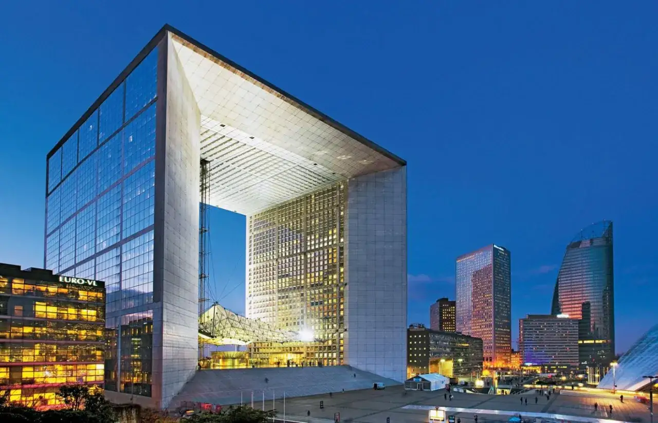 Wielka, nowoczesna brama w Paryżu, La Grande Arche, oświetlona nocą, otoczona innymi drapaczami chmur.