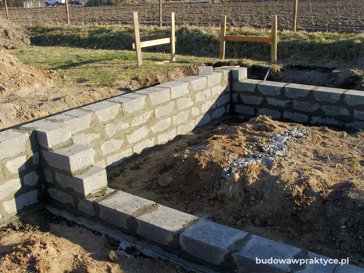 Budowa fundamentów z bloczków betonowych. Ściany z betonu są wznoszone w wykopie, tworząc zarys przyszłego budynku.