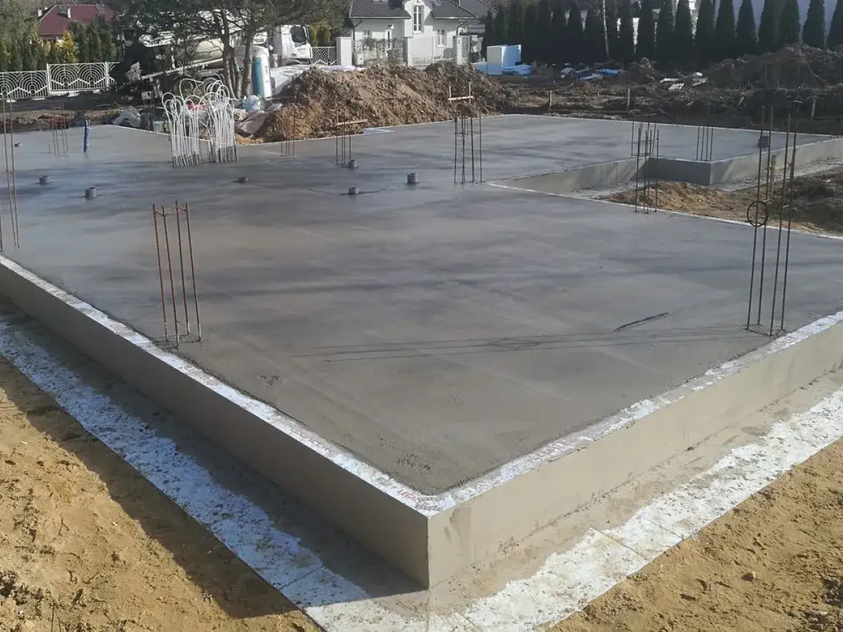 Fundament świeżo wylany, gotowy na dom 100m2. Widać zbrojenie i beton.