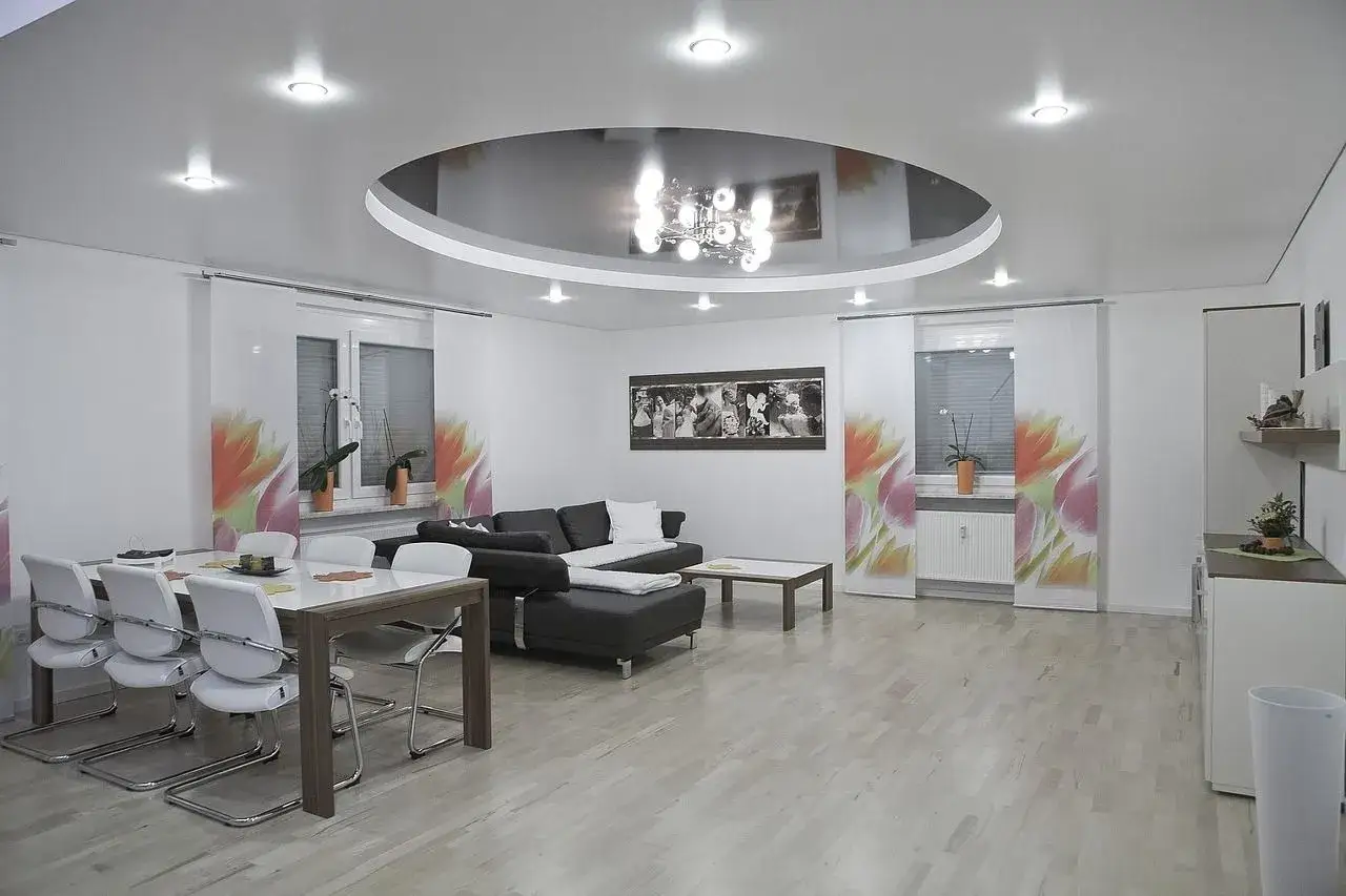 Nowoczesny salon z okrągłym, lustrzanym sufitem napinanym, który odbija elegancki żyrandol.