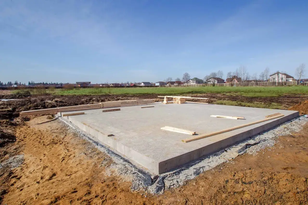 Płyta fundamentowa, jeden z rodzajów fundamentów, gotowa pod budowę domu. W tle domy i niebo.