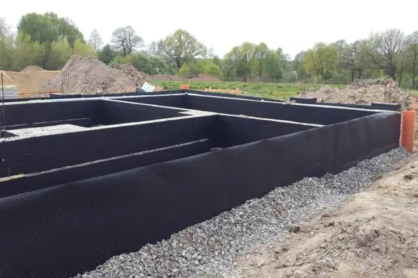 Fundament domu z izolacją przeciwwilgociową. Czarna masa bitumiczna chroni ściany przed wilgocią, a drenażowa membrana zapobiega gromadzeniu się wody.