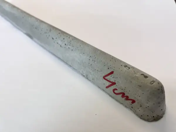 Szary, betonowy element z widocznymi pęcherzykami powietrza, oznaczony czerwonym markerem "4cm". To dystanse do zbrojenia betonowego.