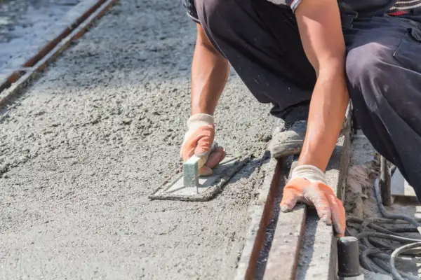 Robotnik wygładza świeży, mokry beton kielnią. Powierzchnia jest jeszcze wilgotna, ale wkrótce stanie się suchy beton.