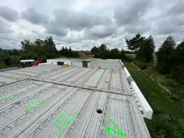 Gotowy do zalania strop żelbetowy, zbrojenie czeka na beton. W tle drzewa i pochmurne niebo.