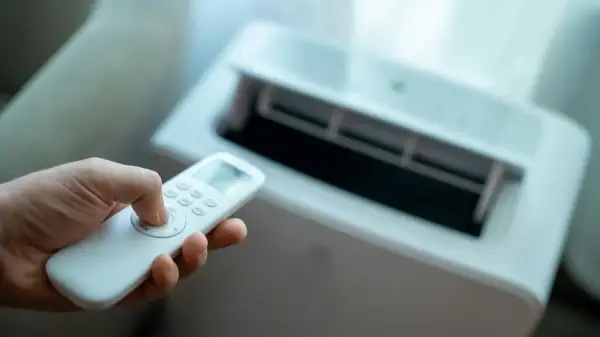 Dłoń trzymająca pilot do klimatyzatora bez jednostki zewnętrznej. Urządzenie chłodzi pomieszczenie.