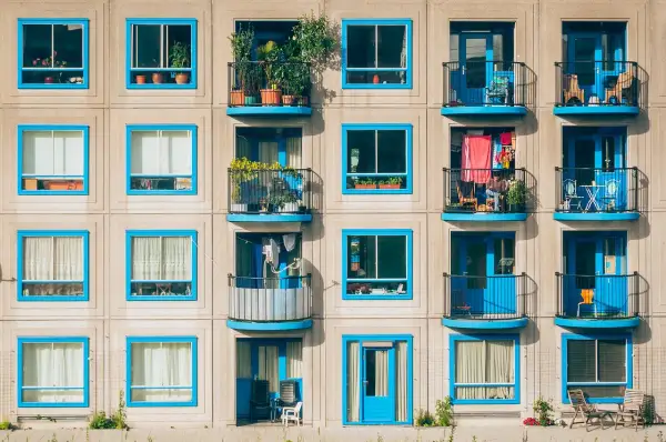 Elegancka loggia i balkon z niebieskimi ramami okiennymi, pełne zieleni i suszącego się prania, tworzą barwną fasadę budynku.
