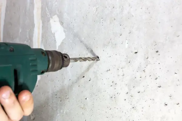 Wiertarka w ręku, rozpoczyna się wiercenie w betonie. Widać postęp prac i przygotowanie otworu.