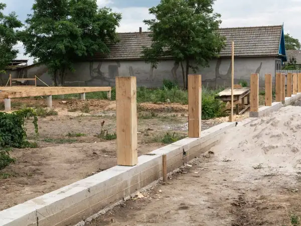 Budowa ogrodzenia: betonowy fundament i drewniane słupki czekają na dalsze prace. Jaki fundament pod ogrodzenie jest najlepszy?