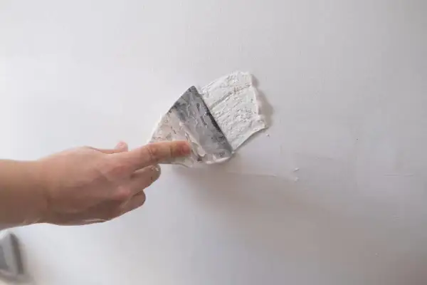 Dłoń zacierająca gips szpachlowy na białej ścianie. Czas, ile schnie gips szpachlowy, zależy od warunków.