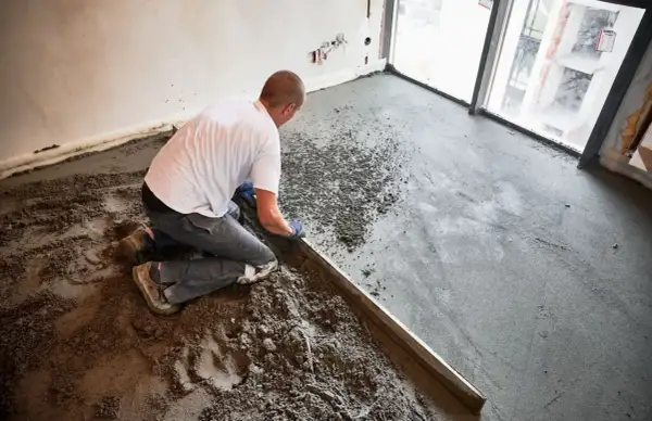 Budowlaniec wyrównuje wylewkę z **anhydrytu** za pomocą łaty.