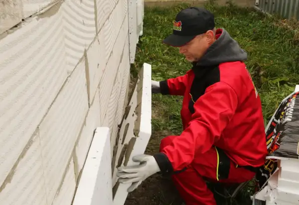Budowlaniec w czerwonym stroju montuje płyty styropianowe na ścianie fundamentowej, zastanawiając się, jakiej grubości styrodur na fundamenty będzie najlepszy.