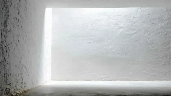 Białe, chropowate ściany i sufit w minimalistycznym wnętrzu z jasnym światłem.